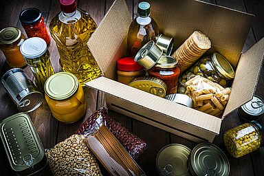 Cardboard box filled with non-perishable foods on wooden table. High angle view.